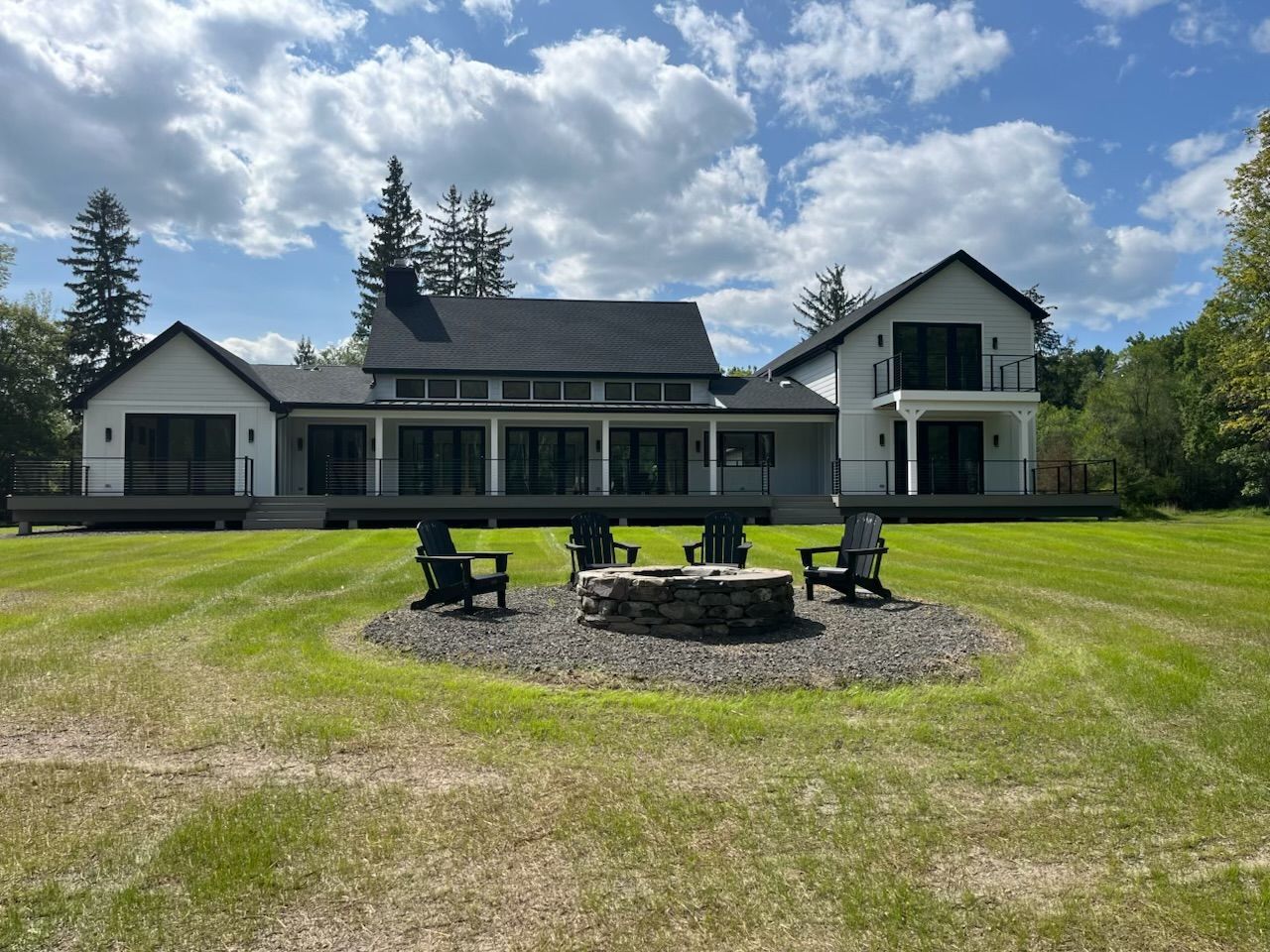 Circular brick patio with two curved wooden benches, fire pit in center, sunny outdoor setting.