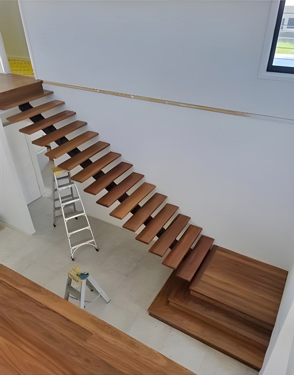 A Wooden Staircase is Being Built in a House With a Ladder Next to It — European Floor Sanding In Mount Louisa, QLD