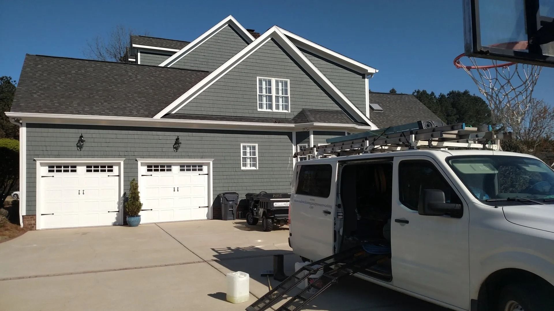 Gray house with two white garage doors, parked white van, and clear blue sky.