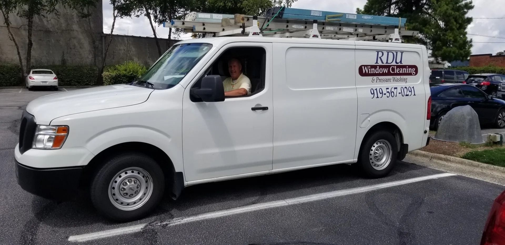 White utility van parked in a lot, with a driver visible through the open window.