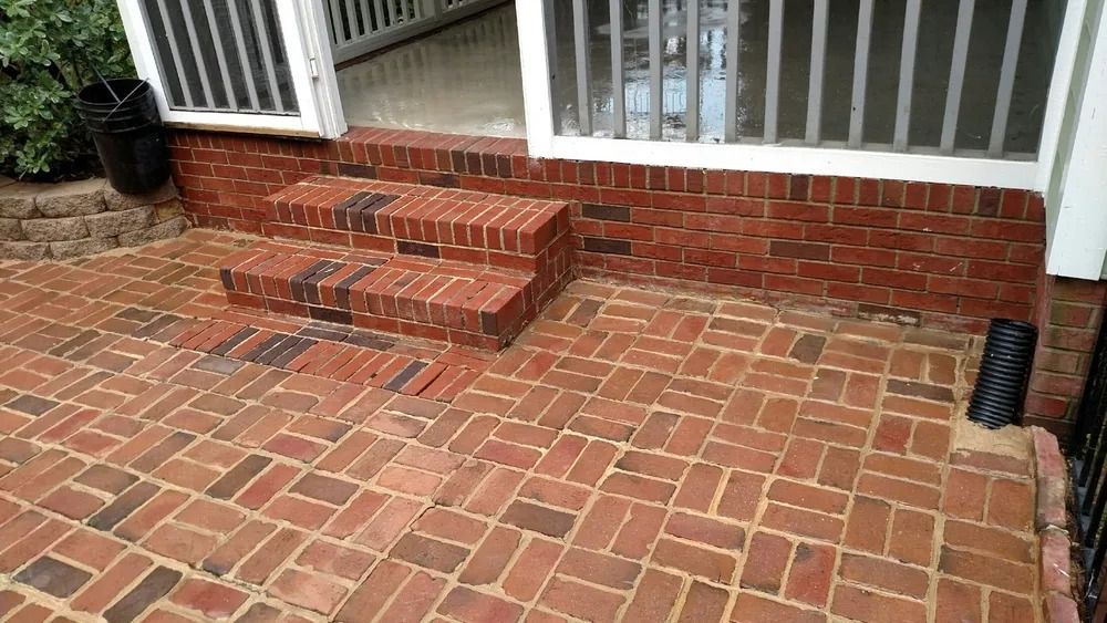 Brick porch with steps, red brick patio, and white railing in front of a house