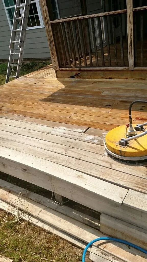 Wood deck being sanded with a yellow floor sander beside a raised porch and railing