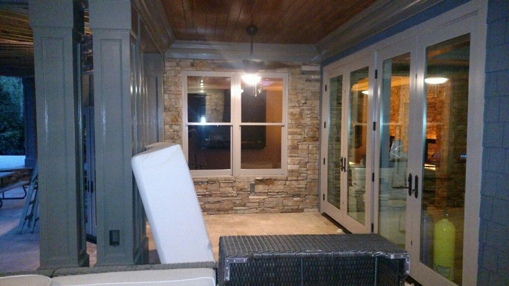 Covered porch with wicker furniture, stone wall, and glass doors at night