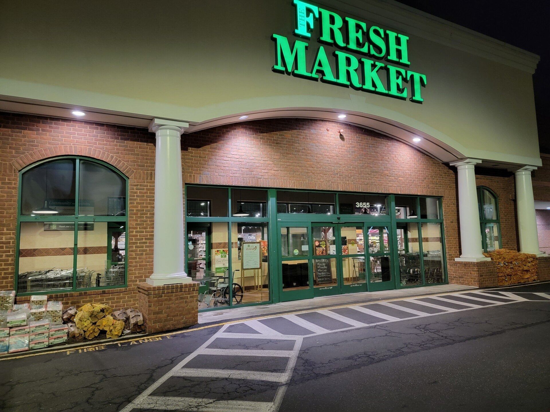 Fresh Market grocery store entrance at night with bright green sign and glass doors