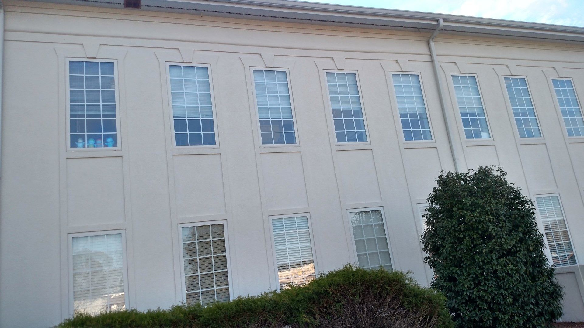 White two-story building facade with many tall windows and bushes in front