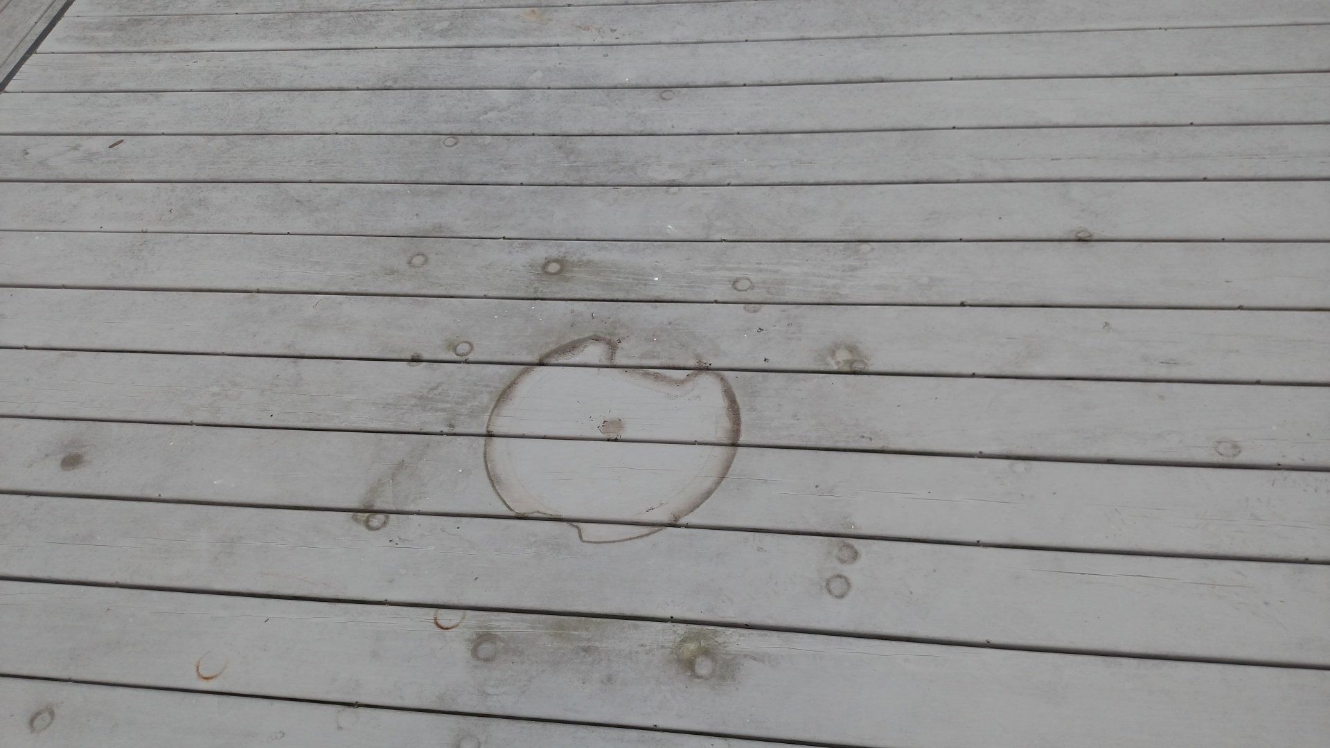 Gray wooden deck boards with a rust-stained ring near the center