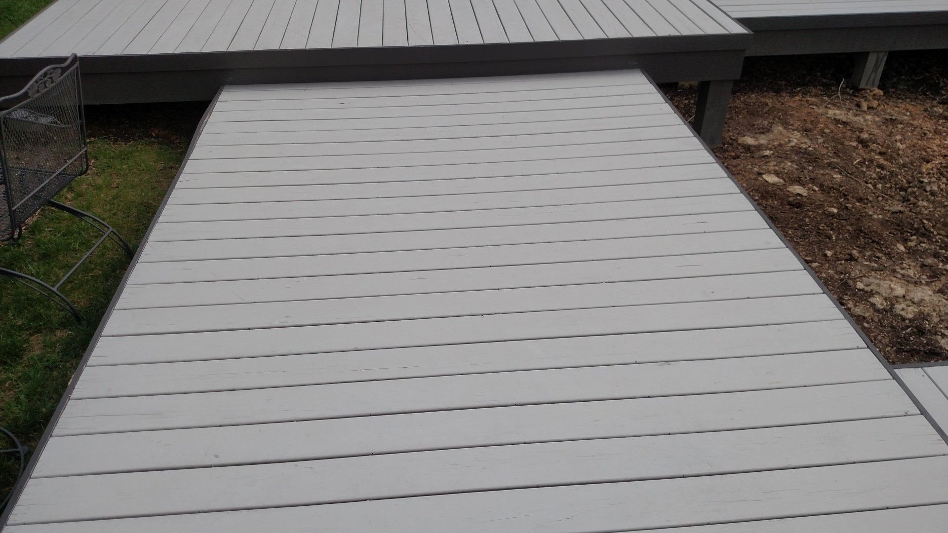 Light gray wooden deck leading to a dark metal-roofed structure outdoors
