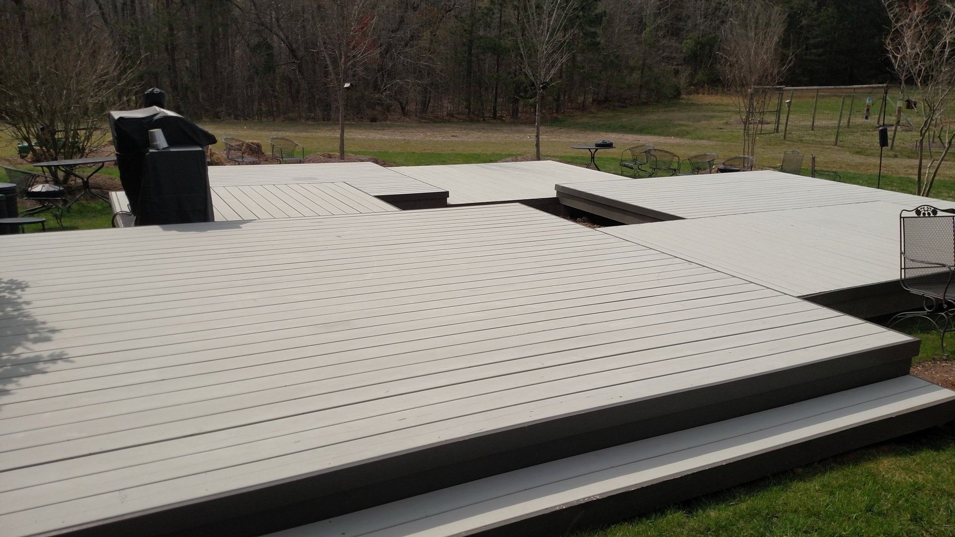 White rooftop with vents and dark trim beside a grassy yard and trees