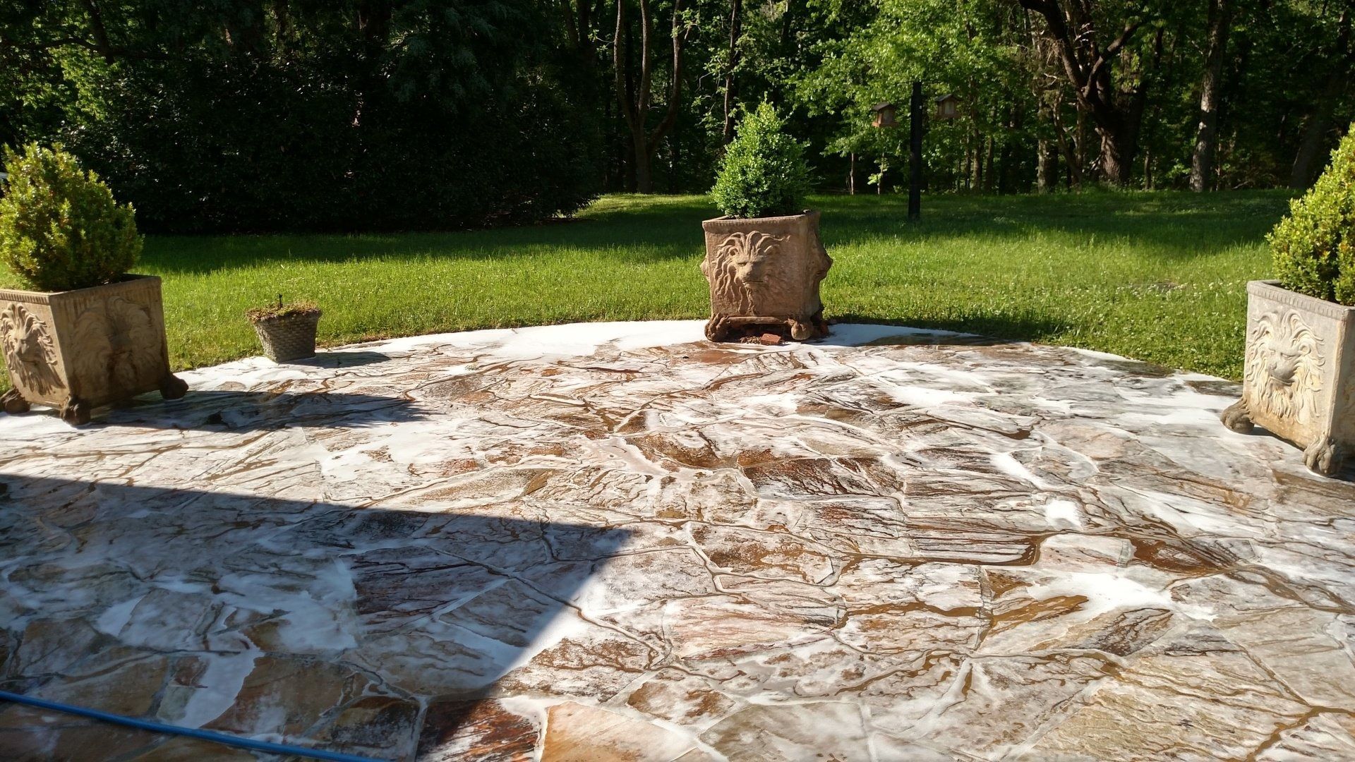 Stone patio with four square stone blocks, bordered by green grass and trees in bright sunlight