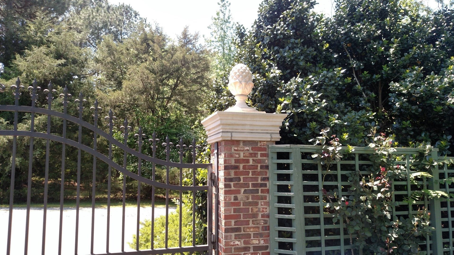 Brick pillar with white bust by a black gate, surrounded by trees and greenery