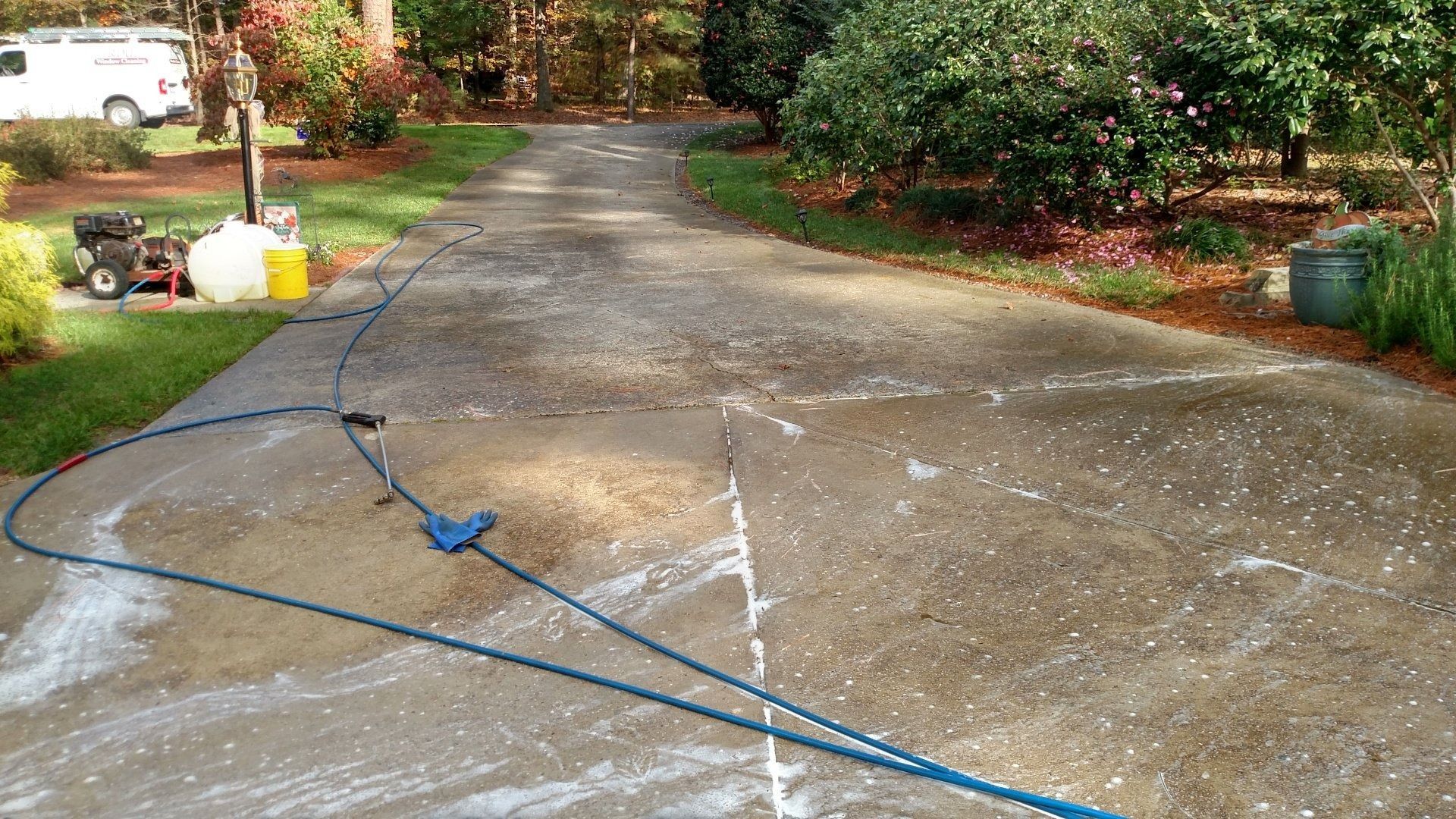 Driveway being pressure washed, with water spray and cleaning equipment in a suburban yard.