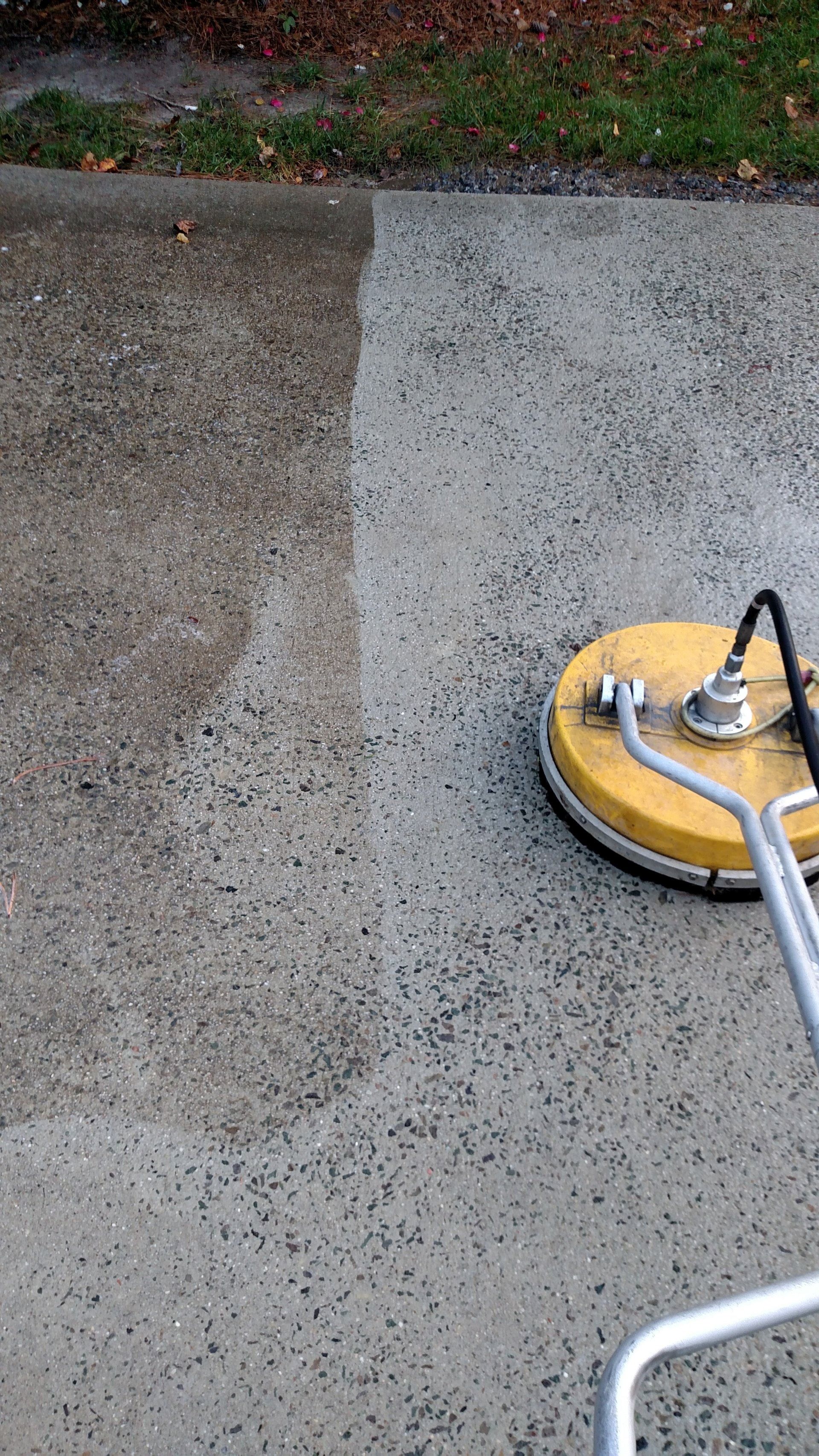 Yellow concrete grinder polishing a wet driveway, leaving a clean gray surface next to rough gravel.