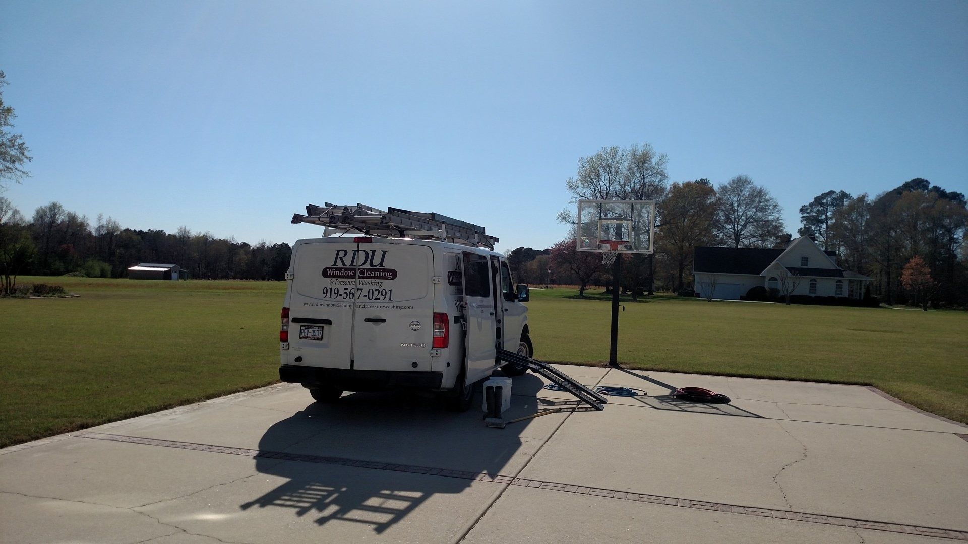White utility van with ladder parked on a driveway in a grassy suburban yard
