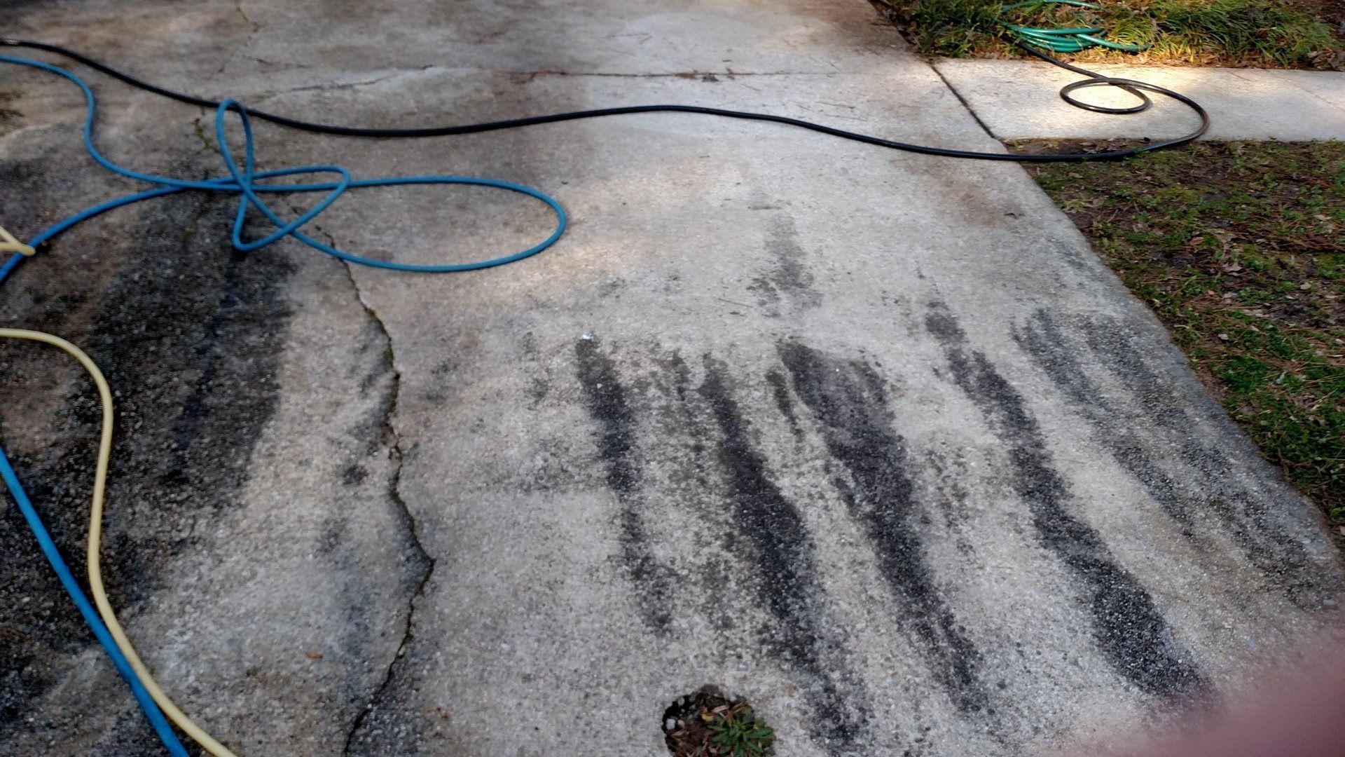 Driveway with dark water stains and blue garden hose coiled on the left side.