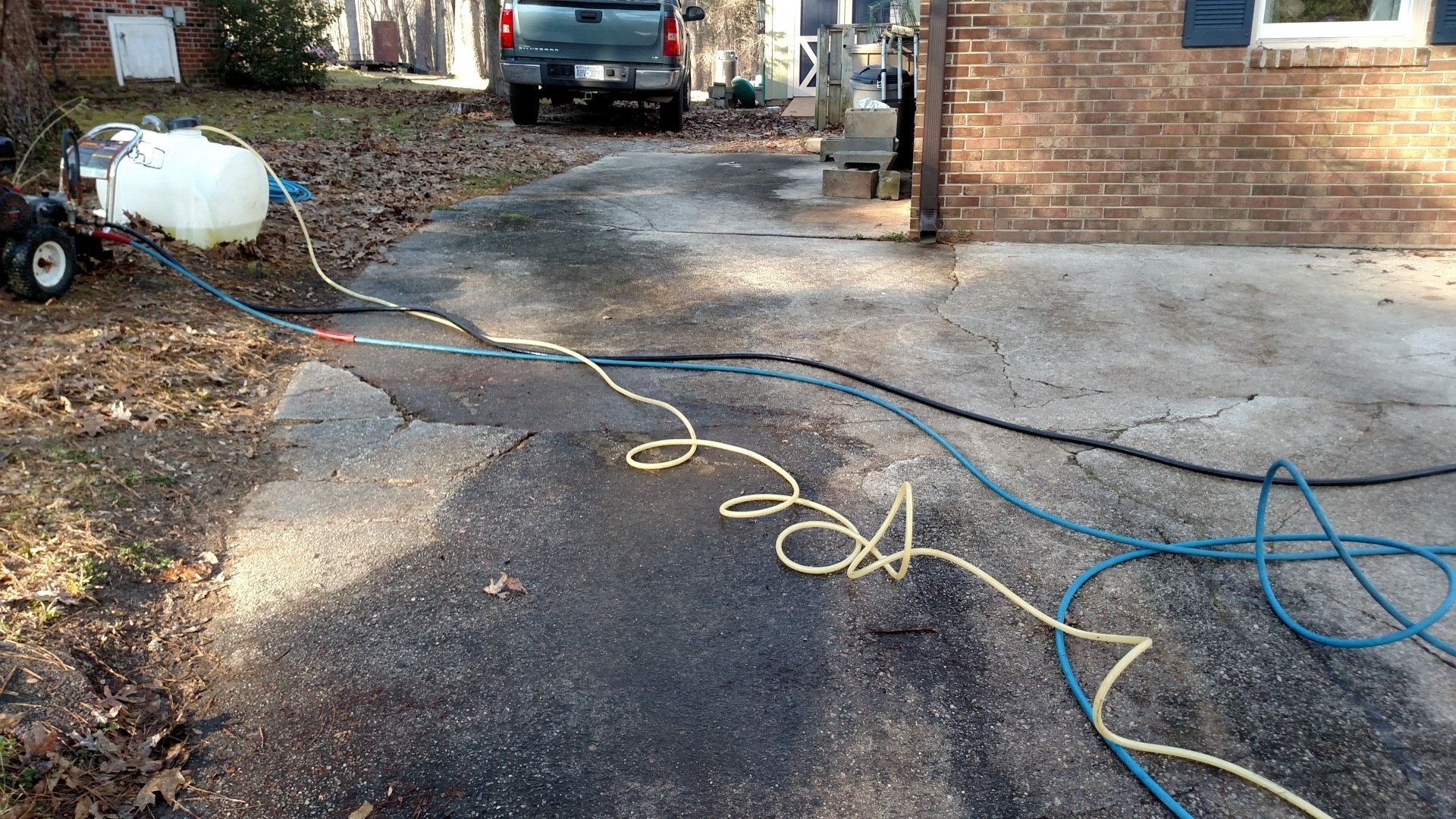 Yellow and blue hoses stretched across a driveway leading to a parked truck and house.