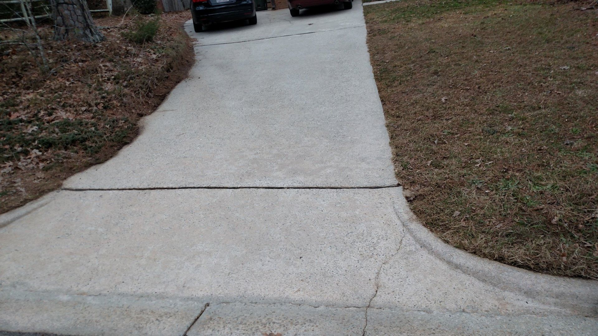 Concrete walkway with a low curb and grass on both sides leading to parked cars.