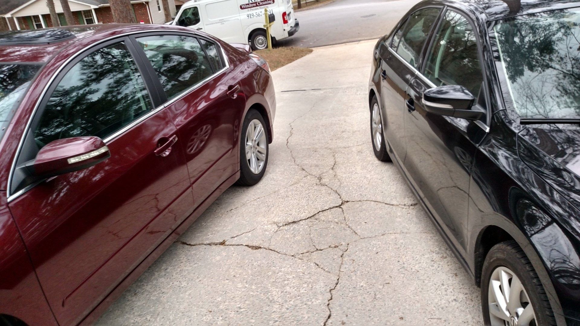 Two parked cars facing a cracked street with a third car in the background.