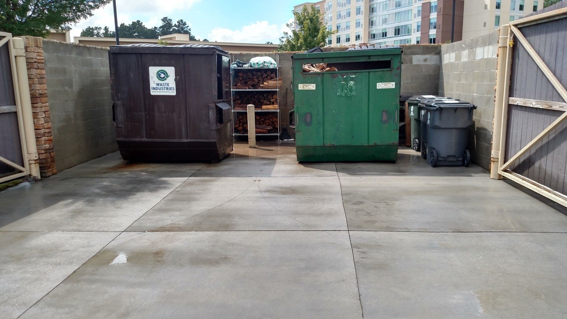 Open courtyard with concrete pavement, dumpsters, and a wooden gate on the right.