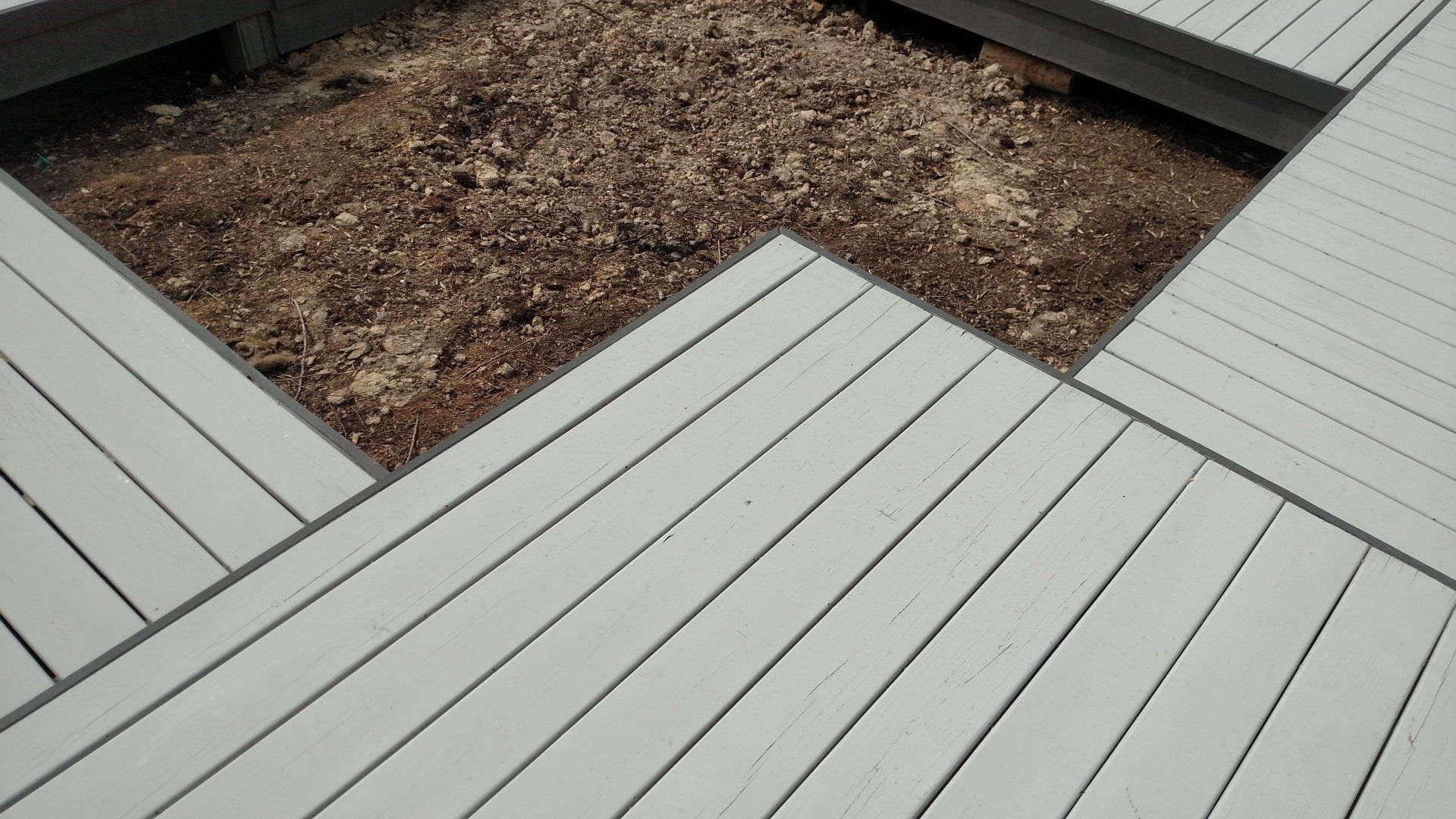 Light gray composite deck framing a raised mulch bed in a geometric outdoor design