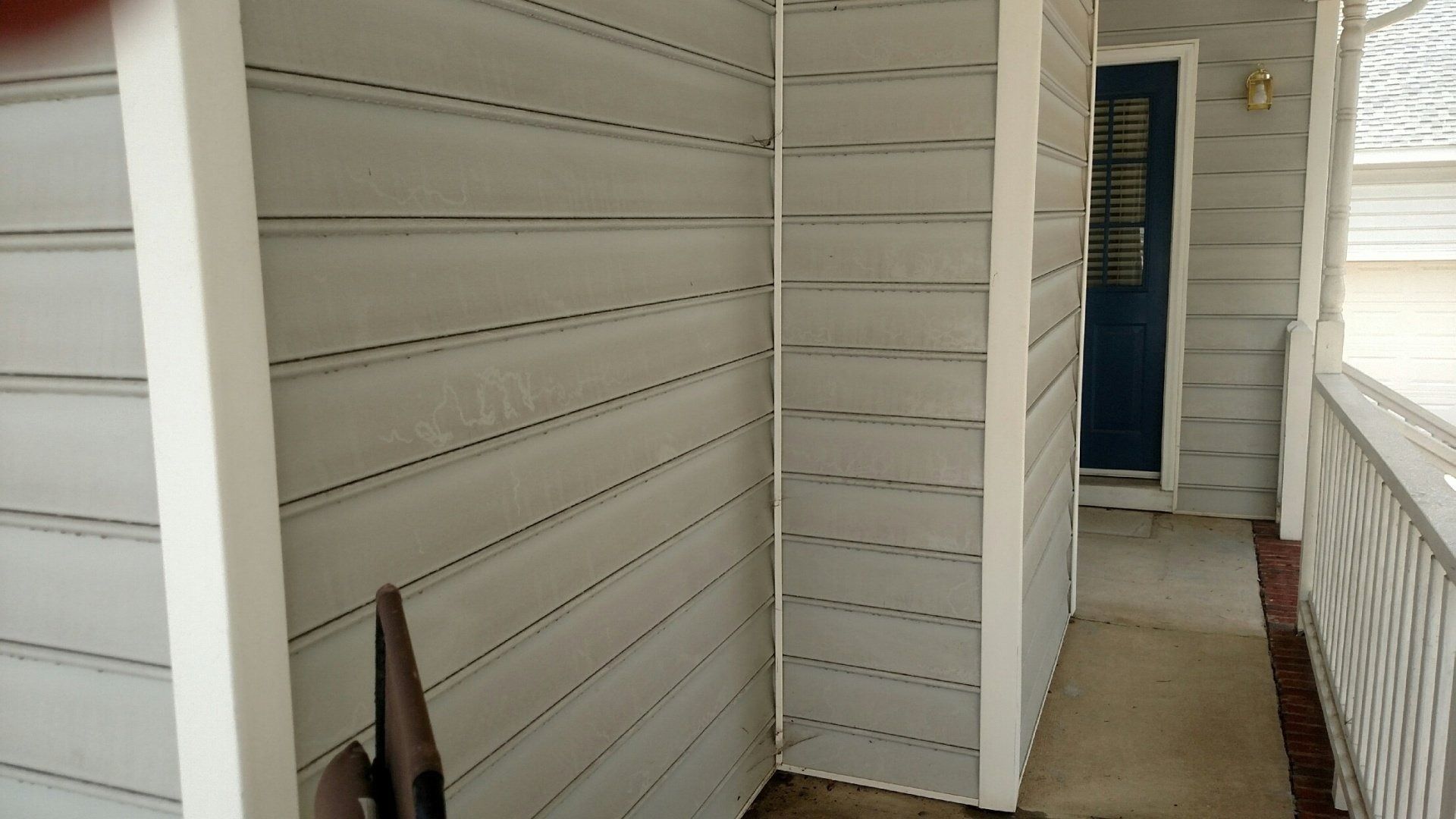 Narrow apartment walkway with white siding, railing, and a blue door at the end.