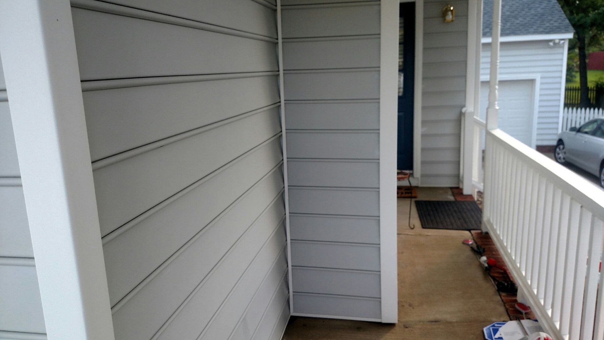 Narrow apartment balcony with beige siding, white railing, and a wet concrete floor.