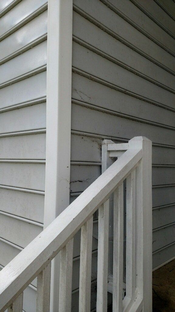 White porch railing beside gray vinyl house siding and a corner post