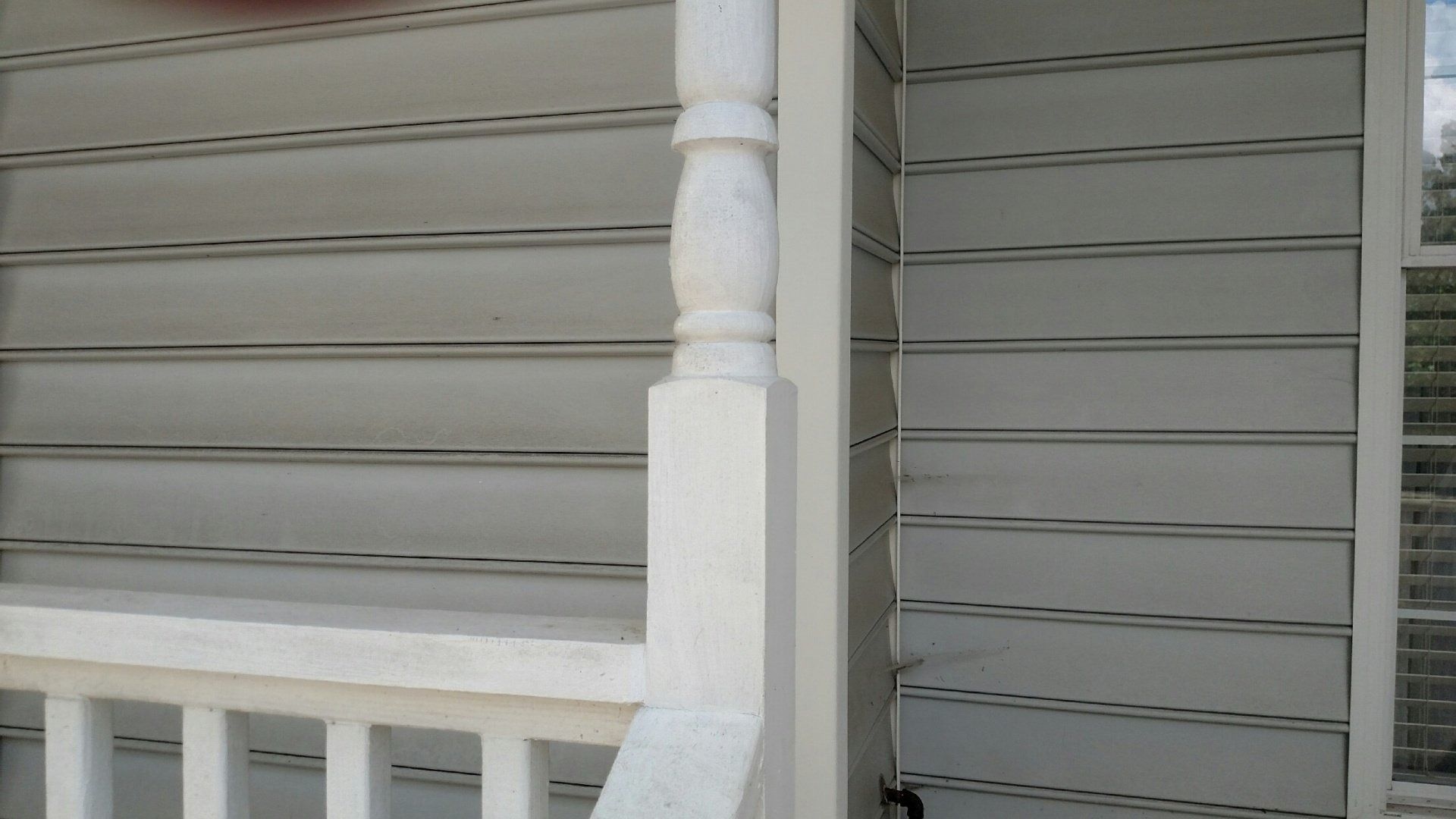 White porch railing and post beside gray vinyl siding and a window shutter