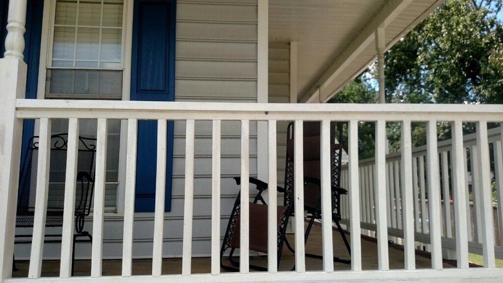 White porch with railings, blue shutters, and a bicycle parked on the shaded deck.