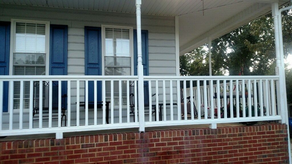 Front porch with white railing, blue shutters, and a brick foundation on a house.
