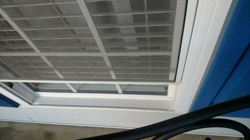Close-up of a white window screen and frame against a blue wall, with a black cable at the bottom