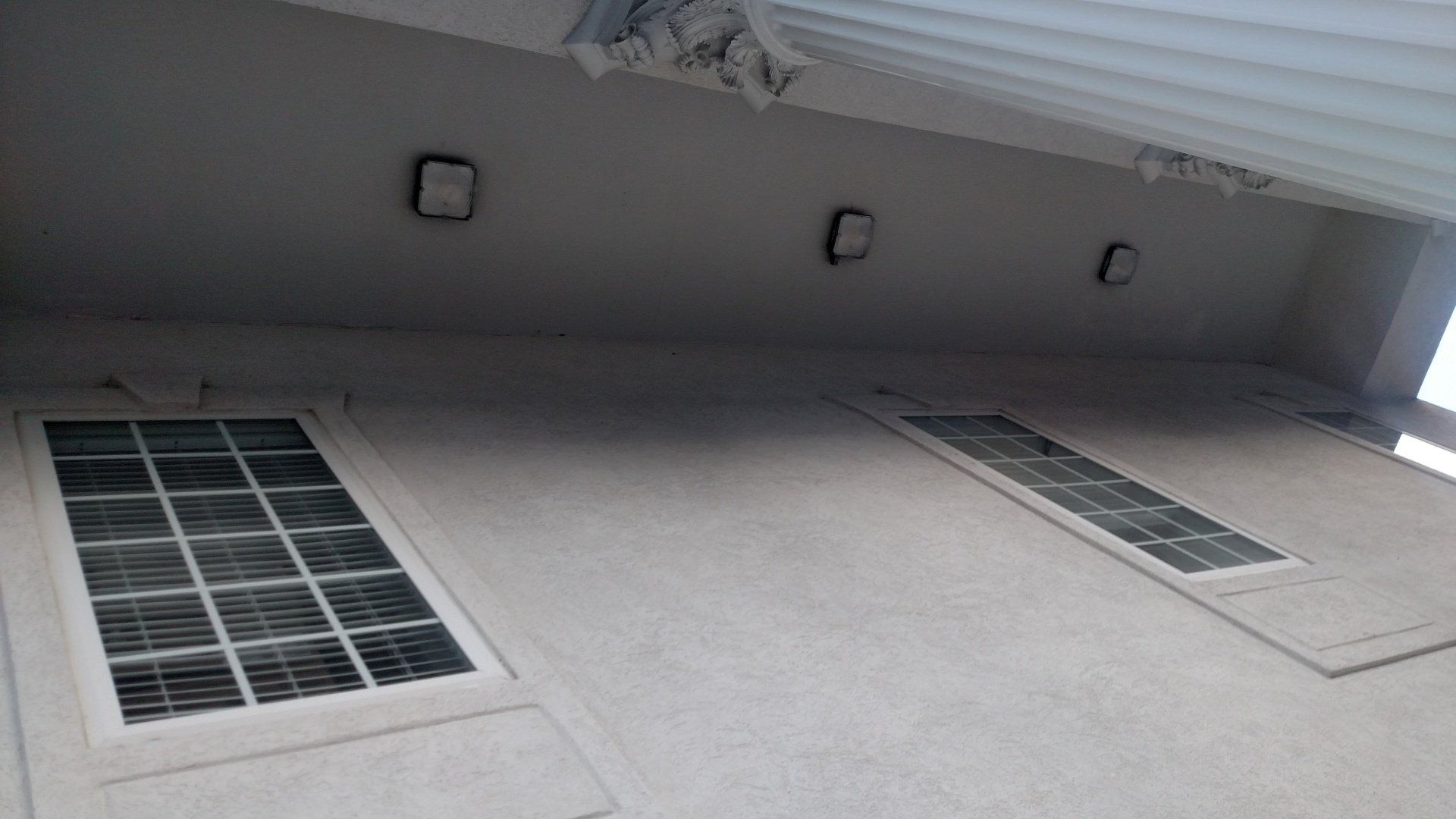 White building wall with two barred windows and three small square lights under an overhang