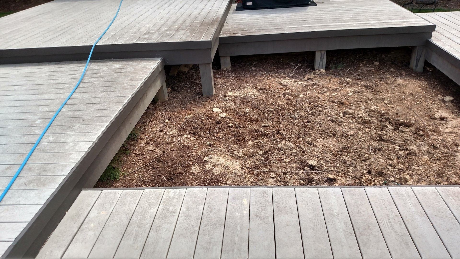 Wooden deck with a rectangular dirt patch in the center, bordered by gray planks and a blue rope on the left.