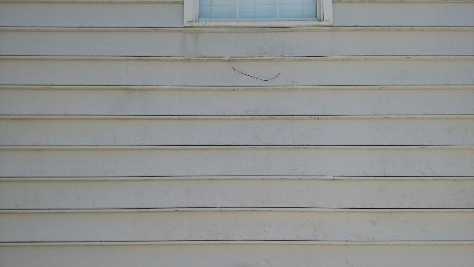 White house siding with a small window near the top and a faint crack below it.