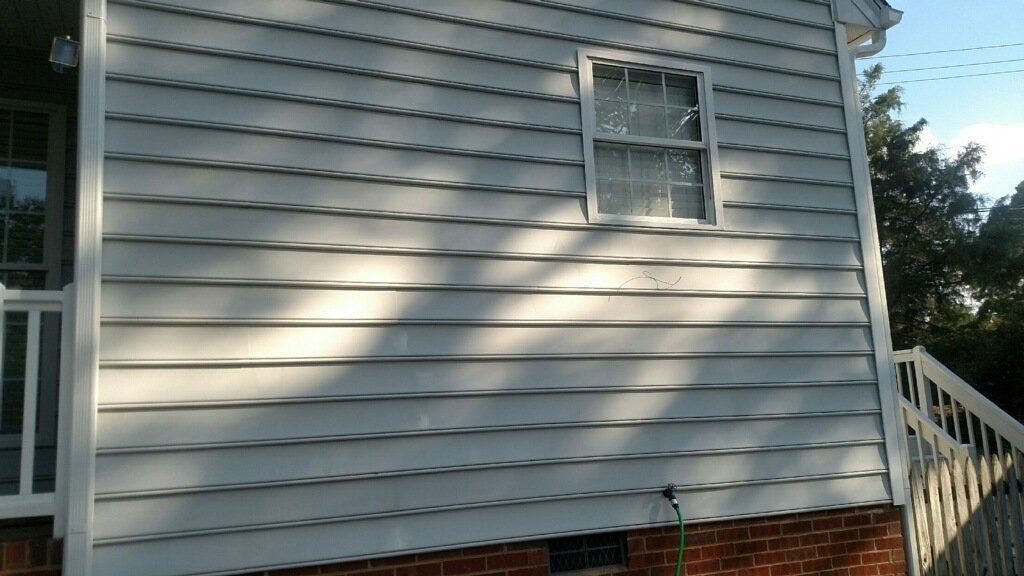 Gray house siding with a small window, brick foundation, and white stairs on the right.