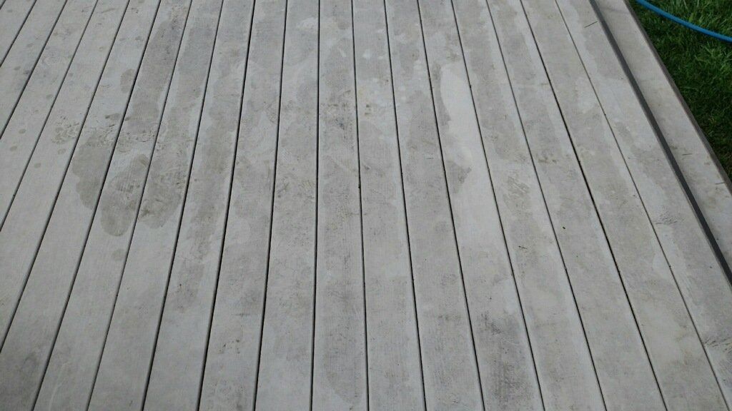 Gray wooden deck boards viewed from above, with dark seams and a strip of grass at the edge