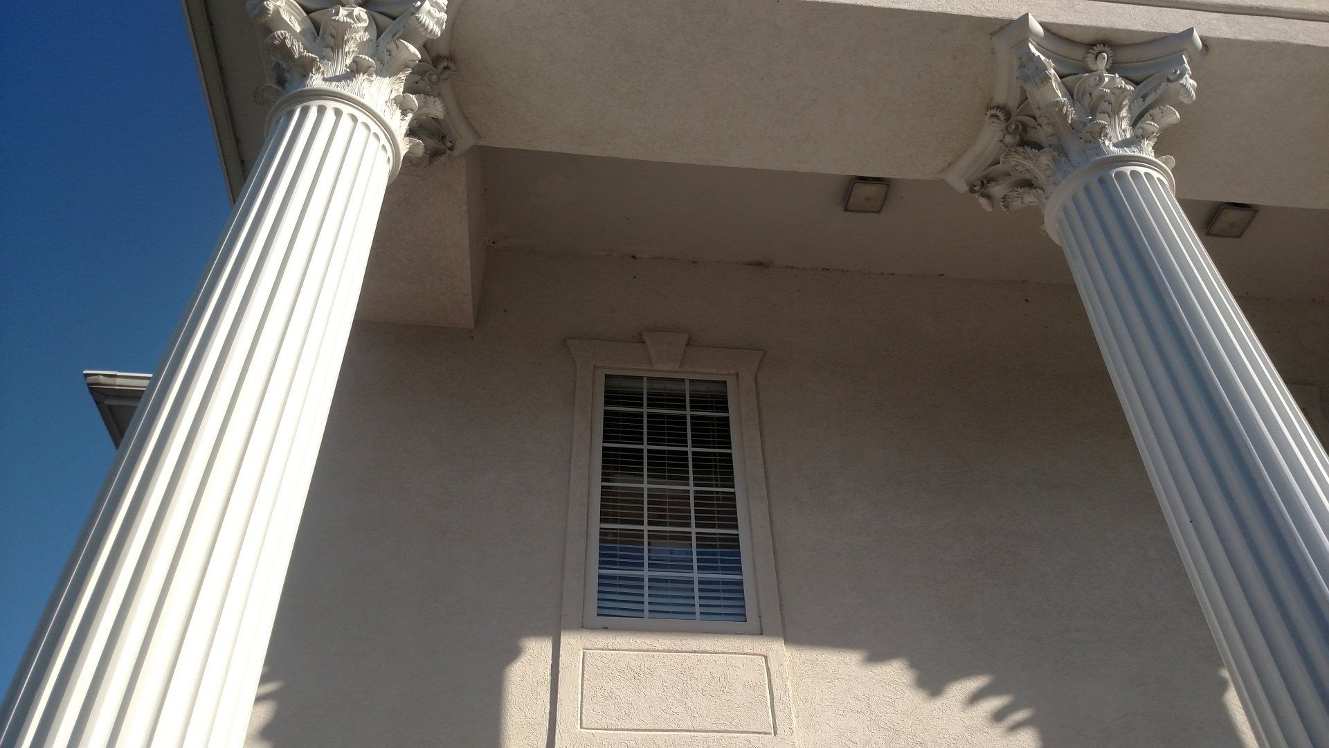 White building facade with two tall columns and a small window beneath a roofline