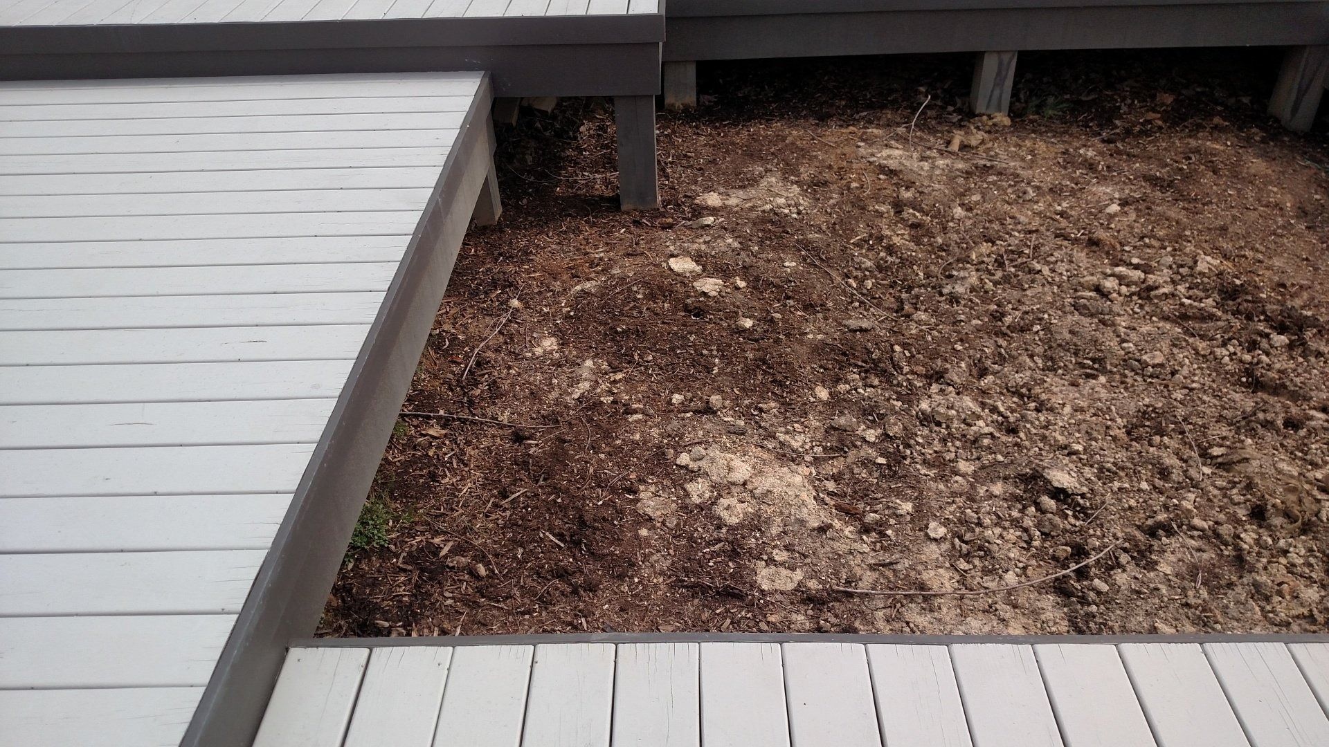 Wooden deck boards framing a mulch bed with a small opening beneath the deck.
