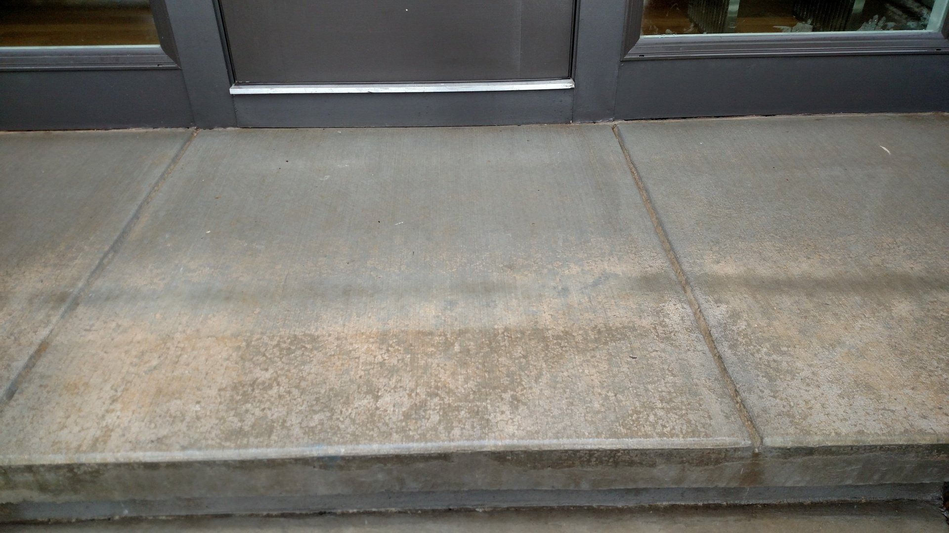 Concrete sidewalk in front of a building entrance with a dark door threshold and curb edge