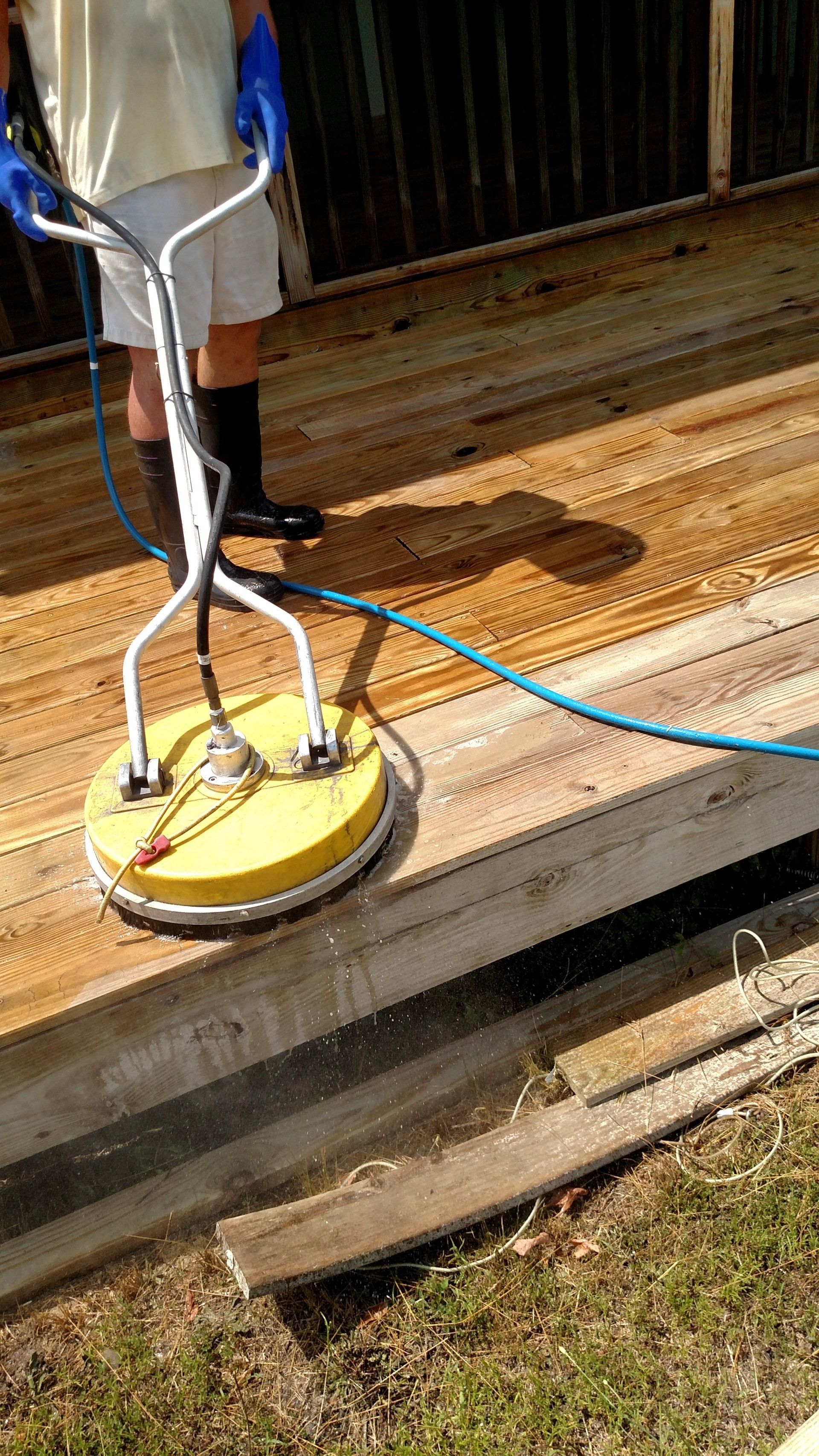 Person using a yellow pressure washer to clean a wooden deck.