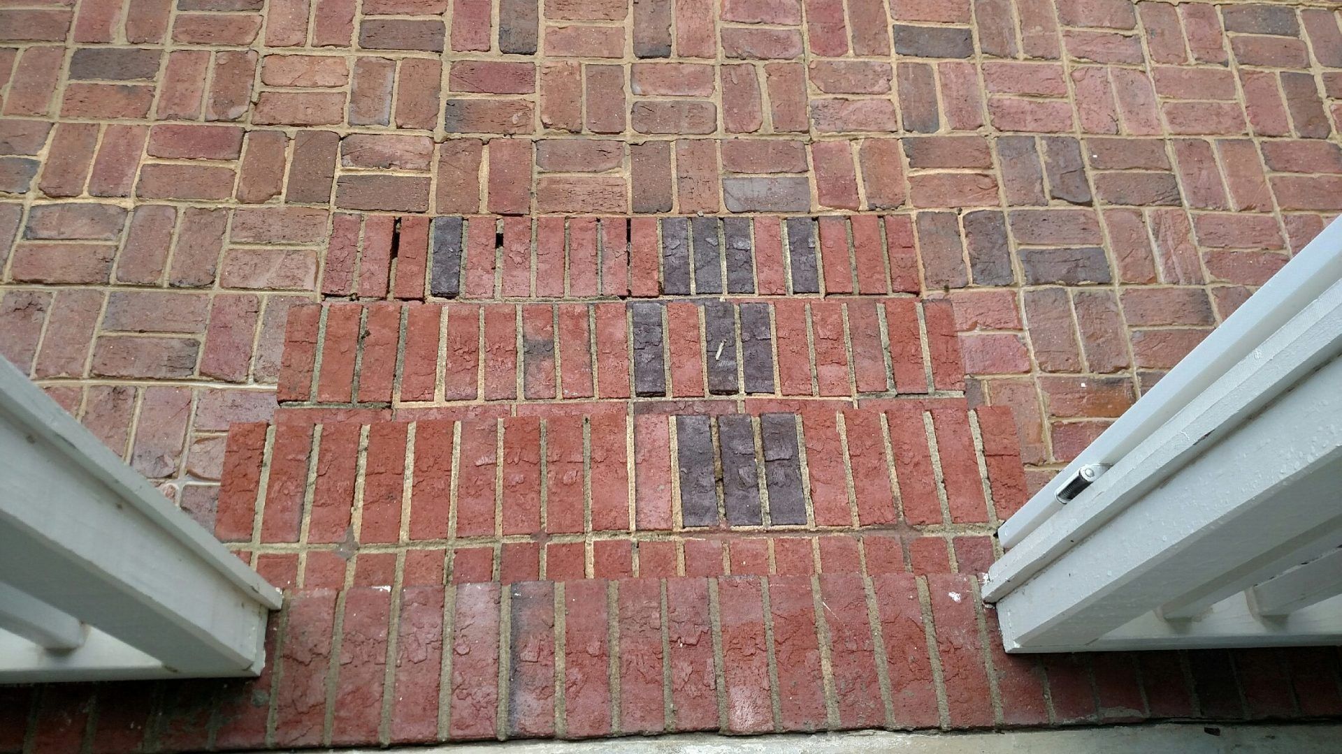 Brick walkway with three dark tactile paving strips between white railings