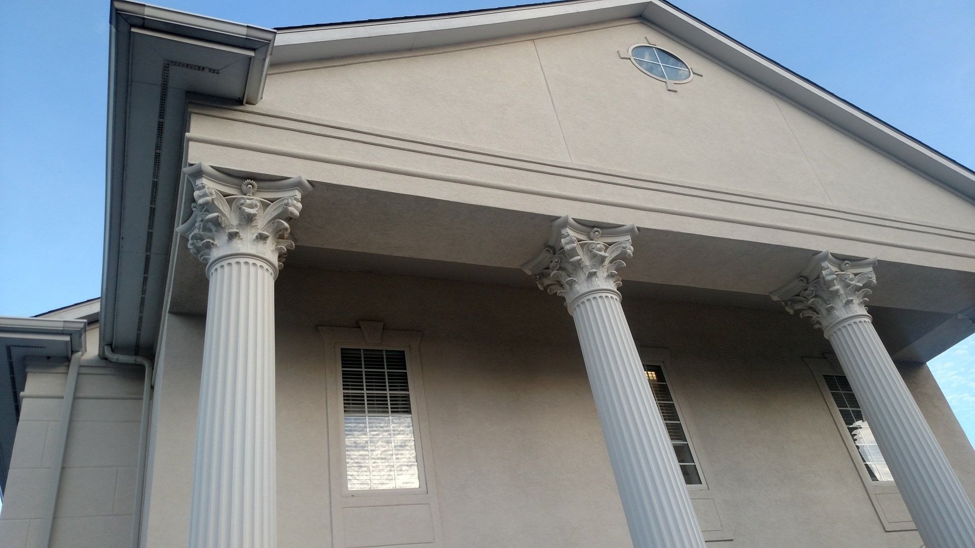Classical building facade with tall white columns and beige walls against a blue sky