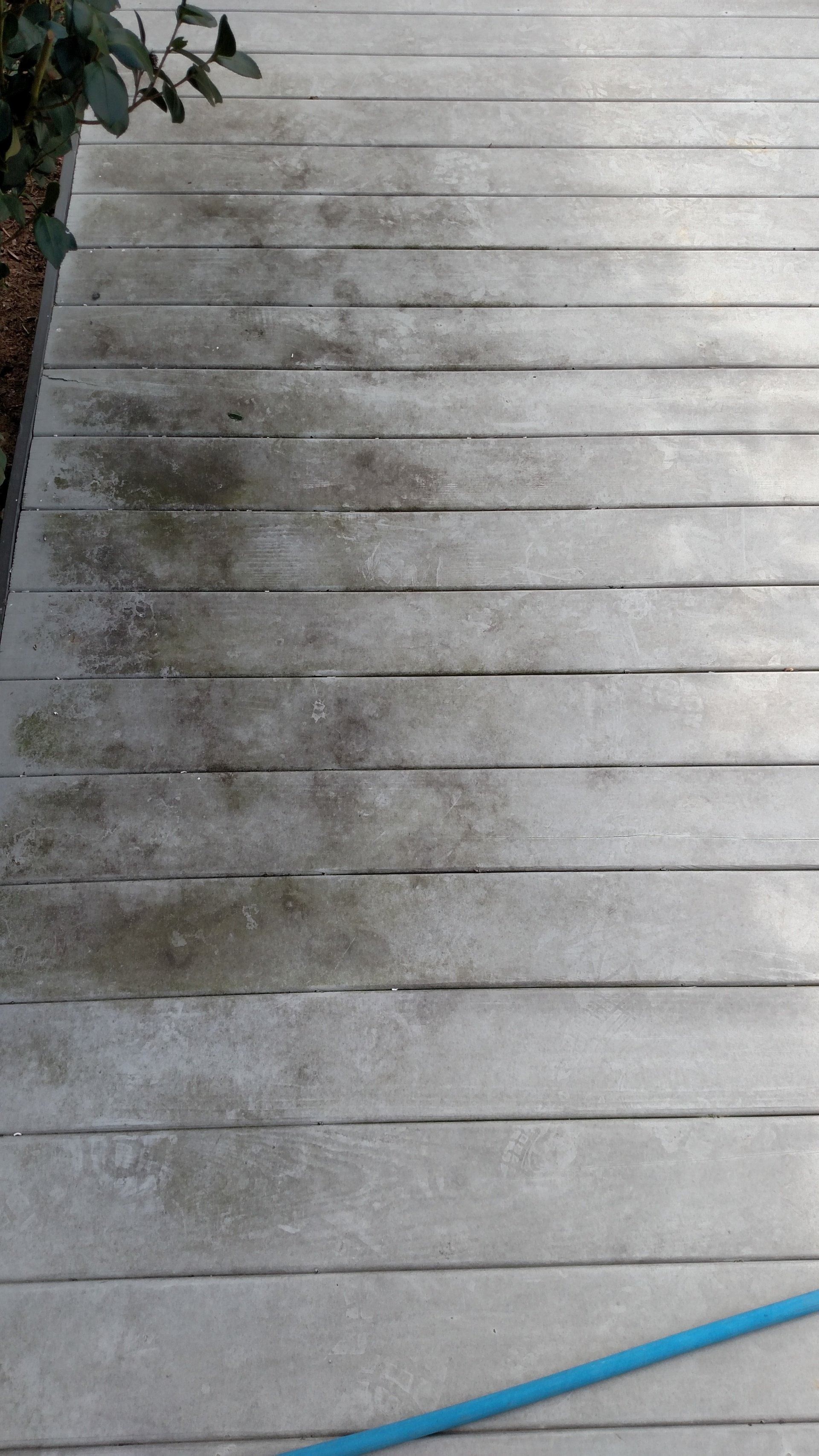 Weathered white wooden deck with dark stains and a blue hose along the bottom edge