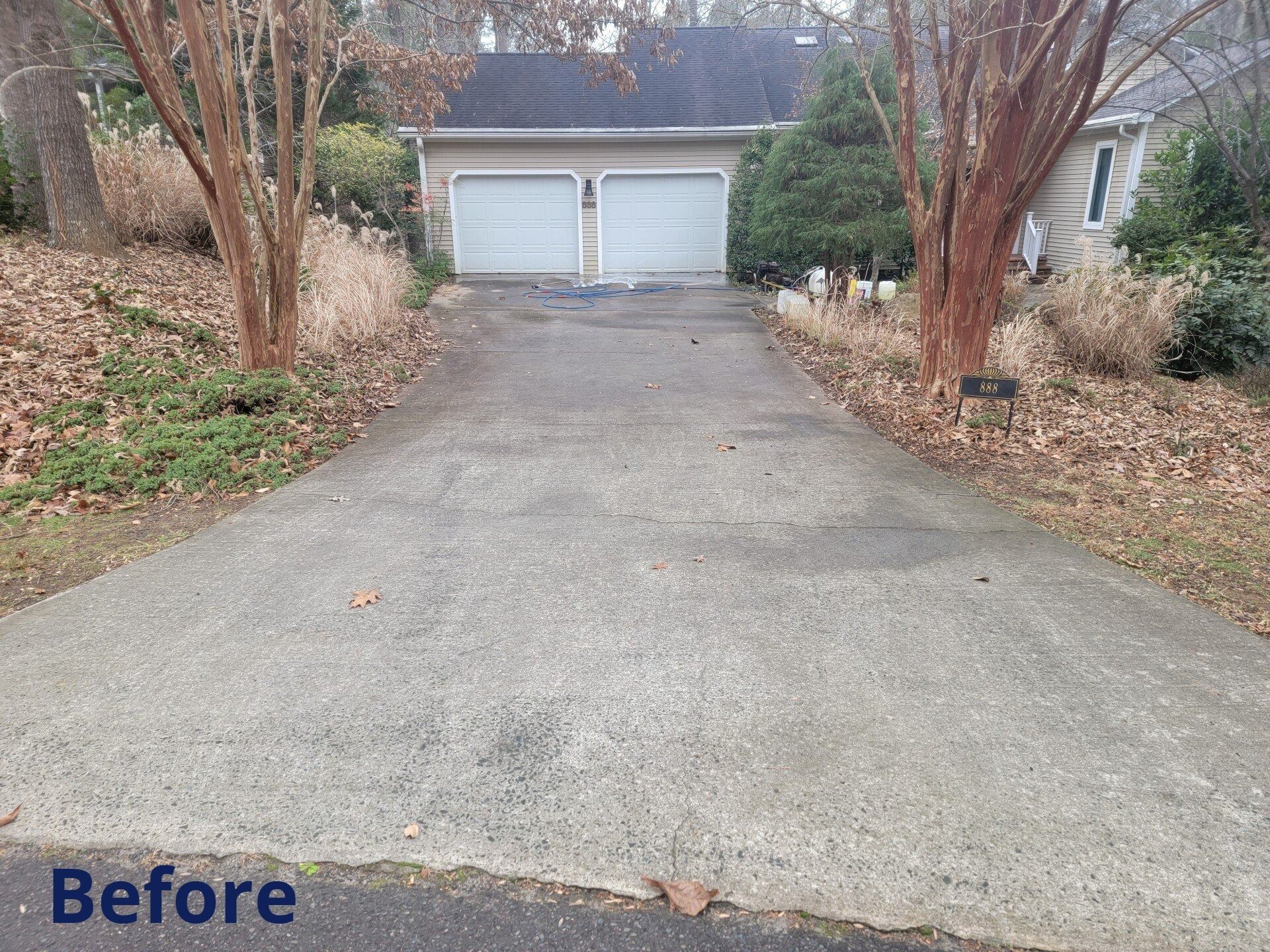 Before view of a sloped driveway leading to a two-car garage with bare trees and winter landscaping