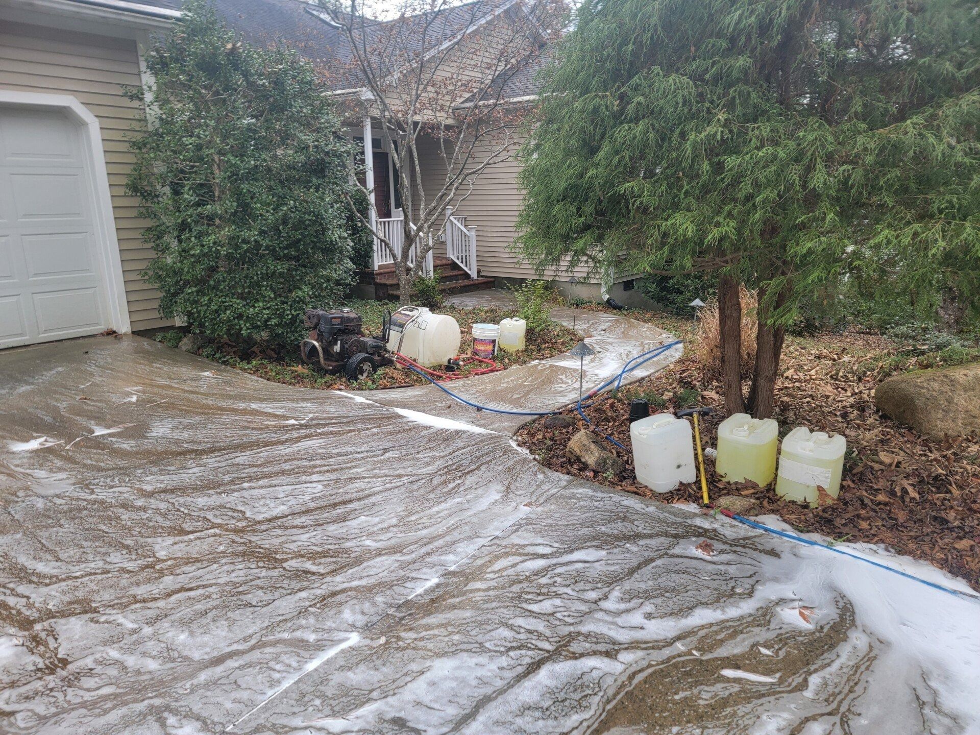 Icy driveway and front yard with snow/ice covering the ground beside a house and garage.