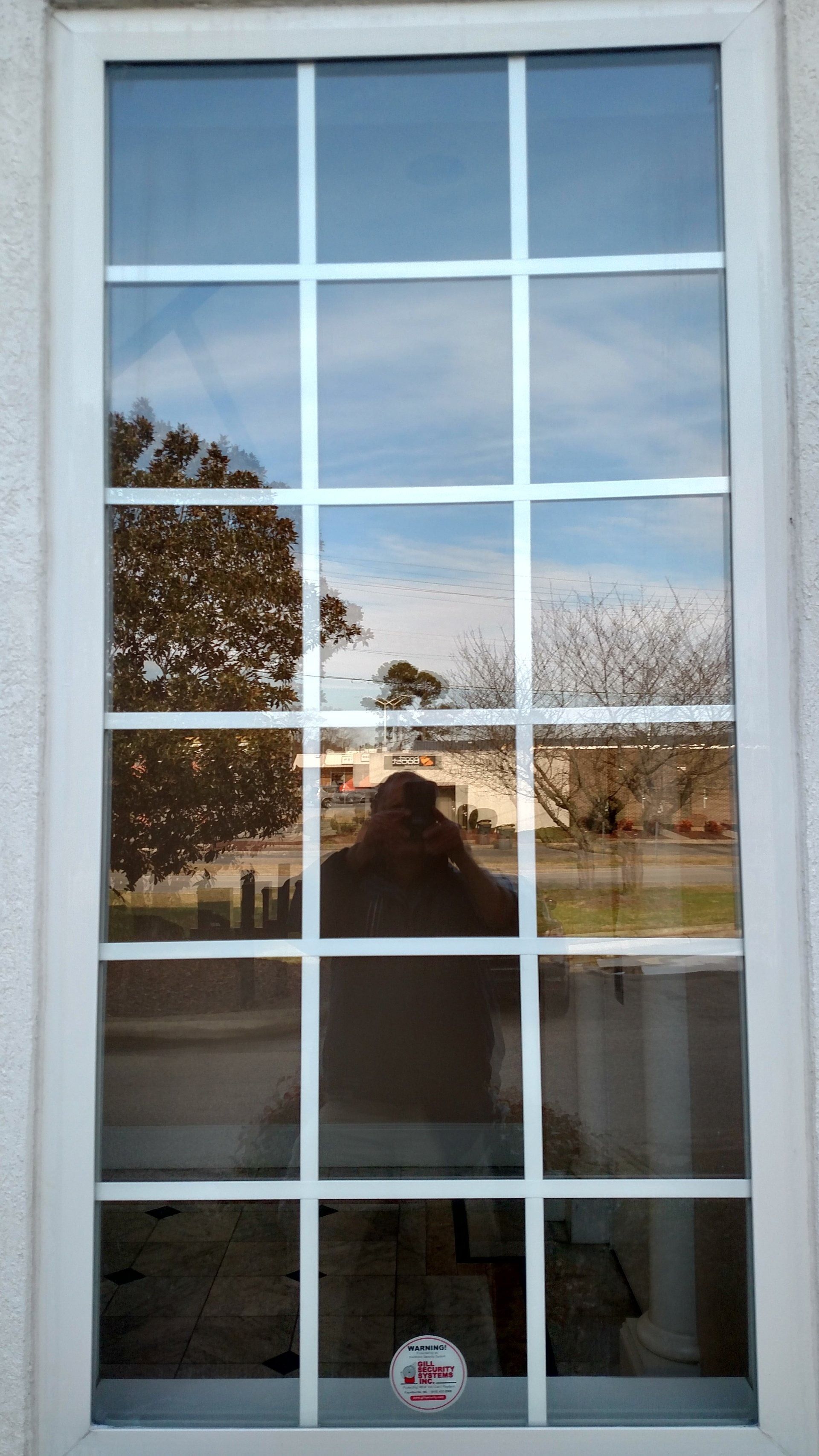 Window with white grid panes reflecting trees, sky, and a walkway outside