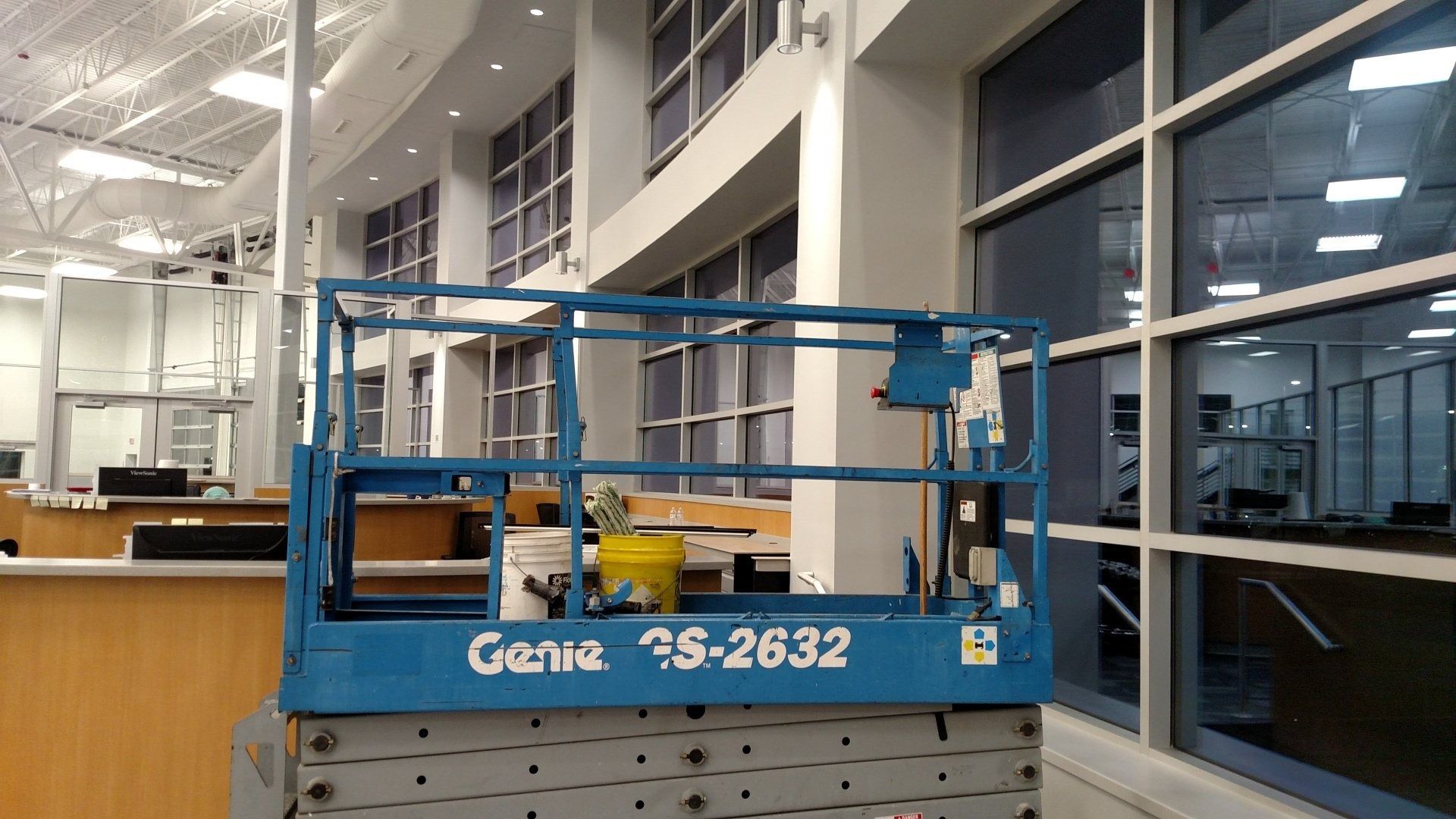 Blue Genie scissor lift parked indoors beside large windows in a warehouse-like space