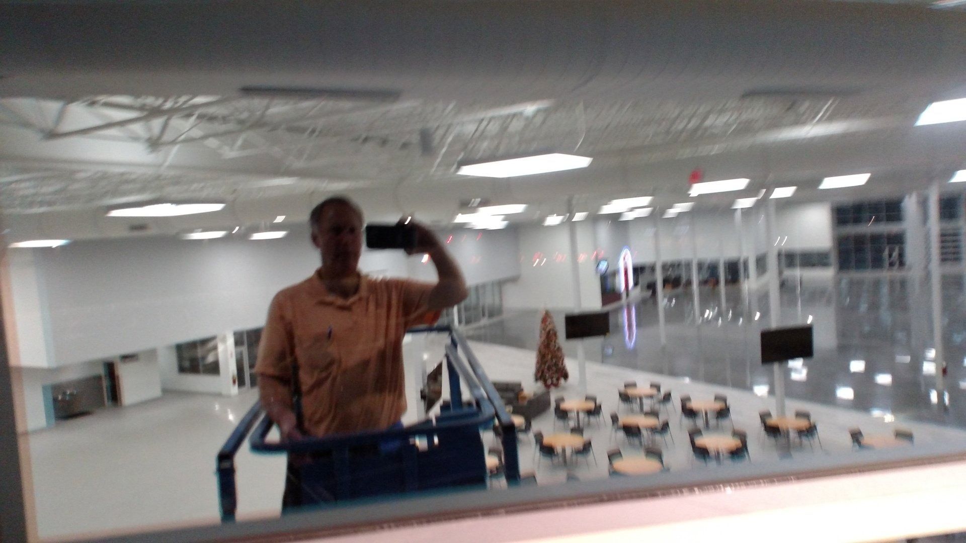 Person taking a mirror selfie in a bright office or showroom with rows of chairs below.