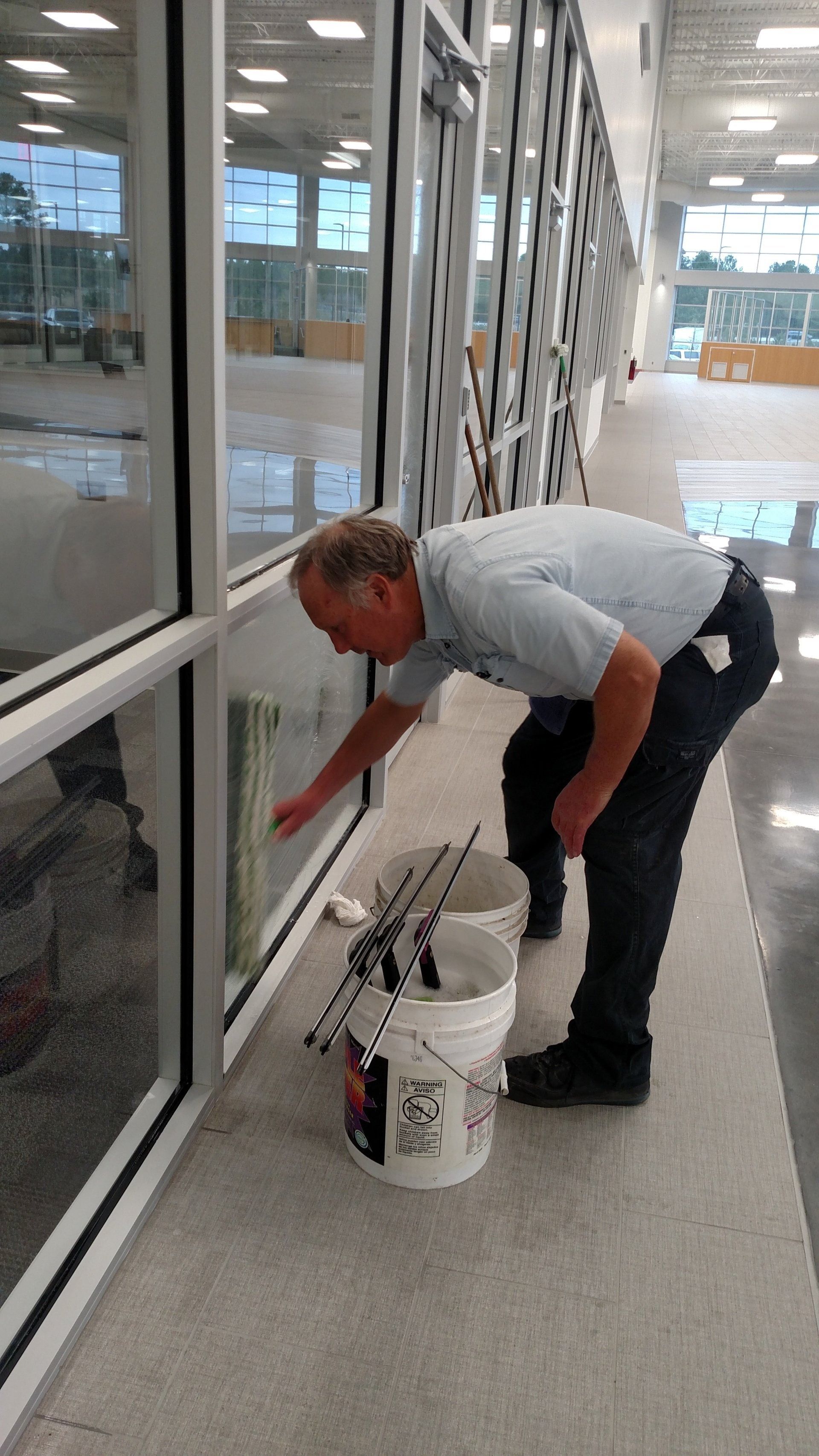 Worker painting a window frame indoors beside a bucket of paint