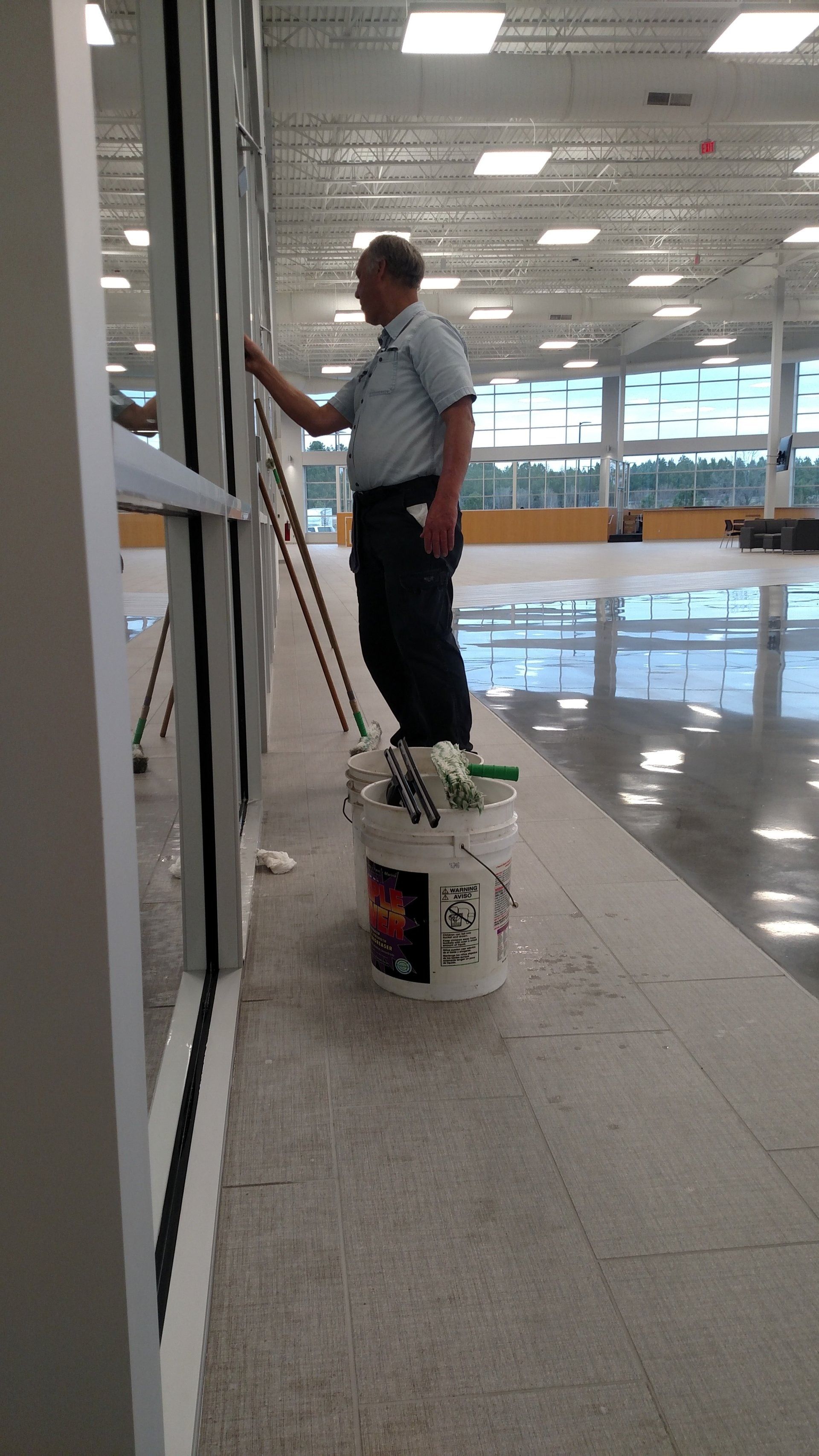 Man standing on a bucket painting a wall in a bright indoor space