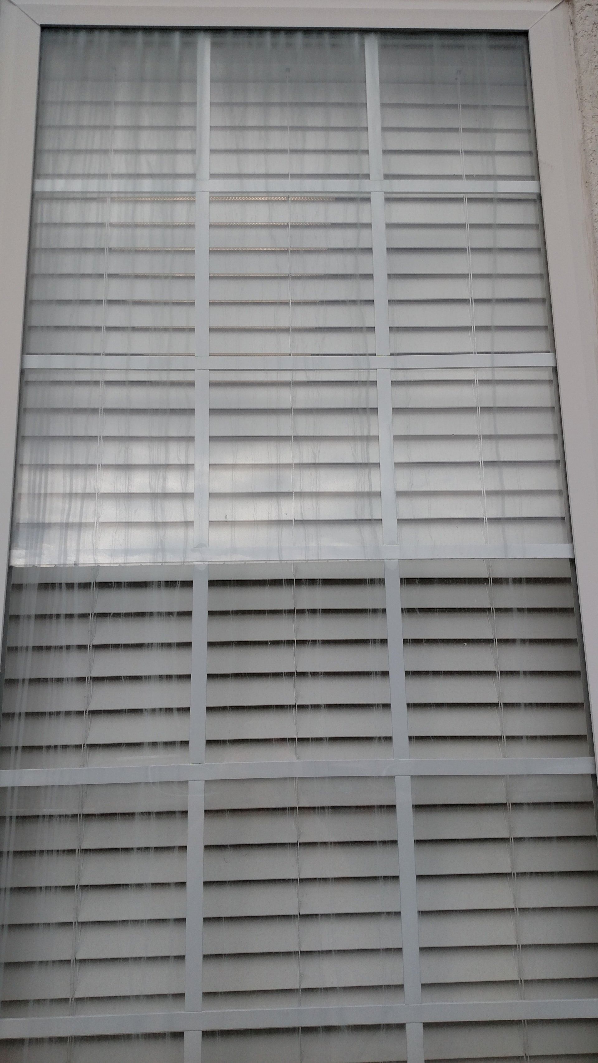 Closed white window blinds on a framed window with a visible damaged or missing slat section near the bottom.